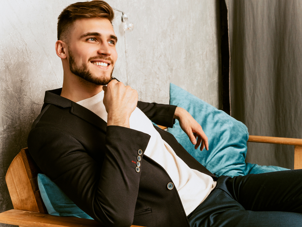 Young man sitting on a couch, smiling confidently after professional dental care – Dentist Southwest Ranches